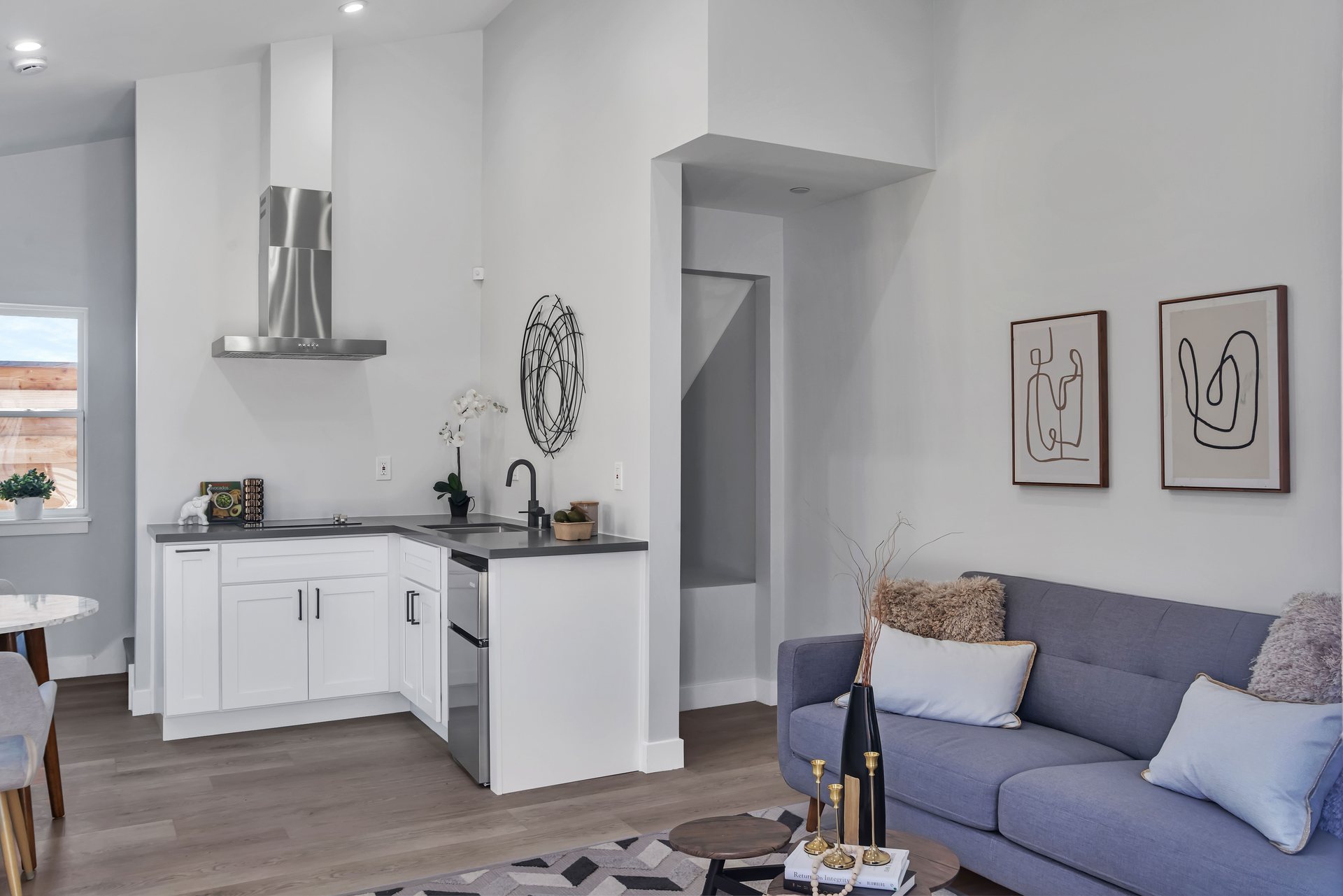 Compact living room with an open kitchenette, stainless wall hood and gray sofa