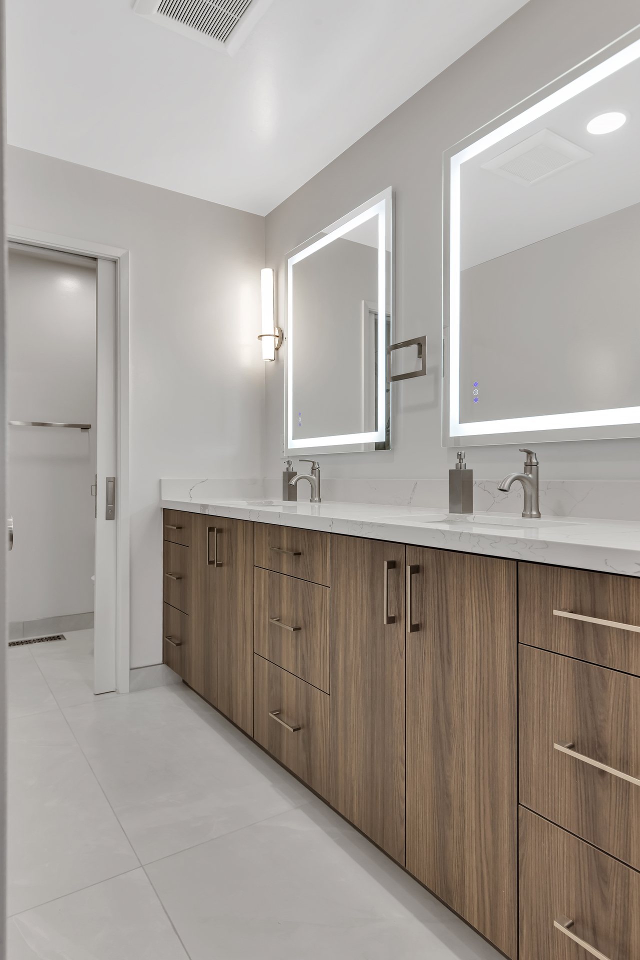 Double vanity with walnut-look cabinets, a quartz countertop and backlit mirrors