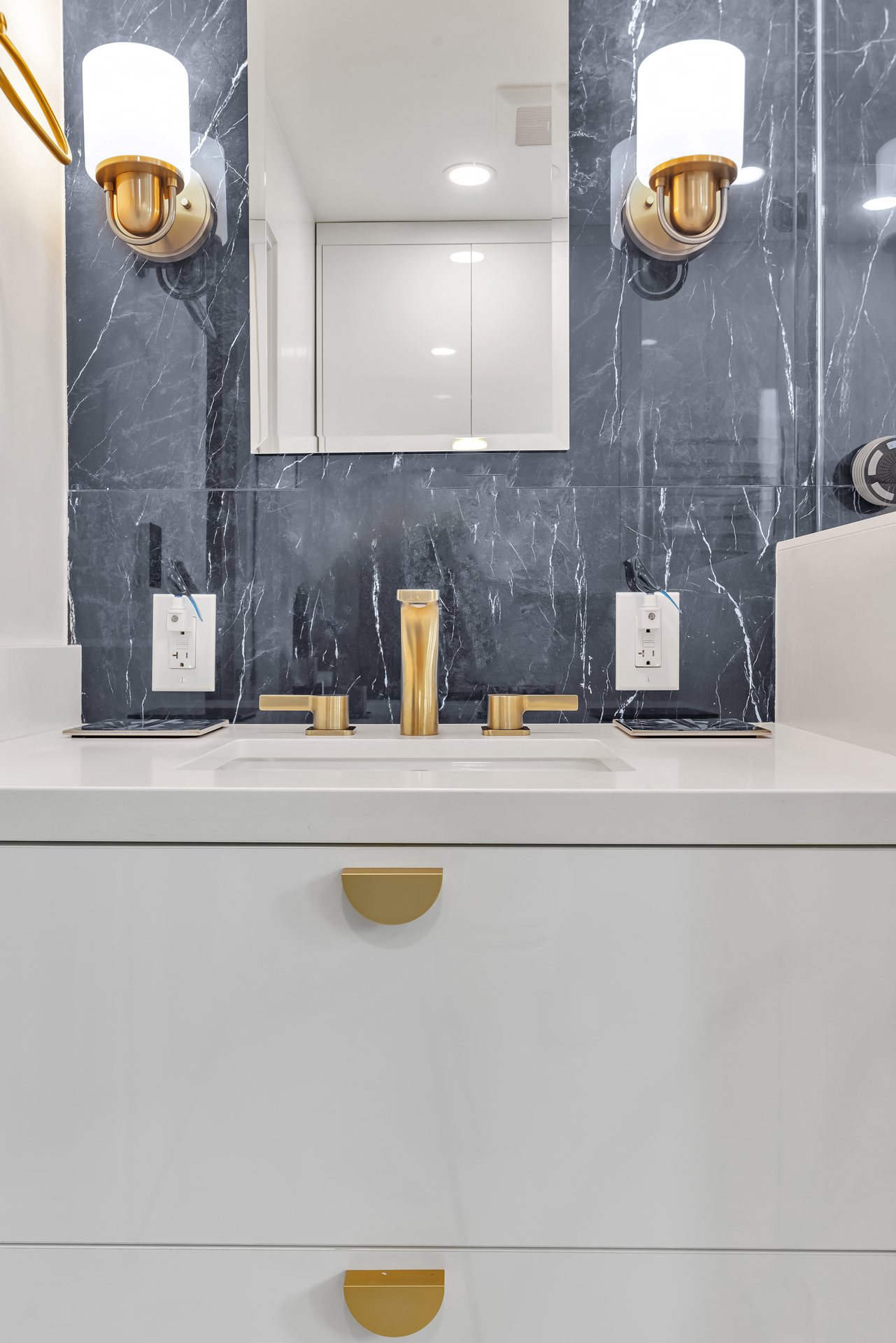 White floating vanity with a brass faucet and sconces against dark marble-look tile