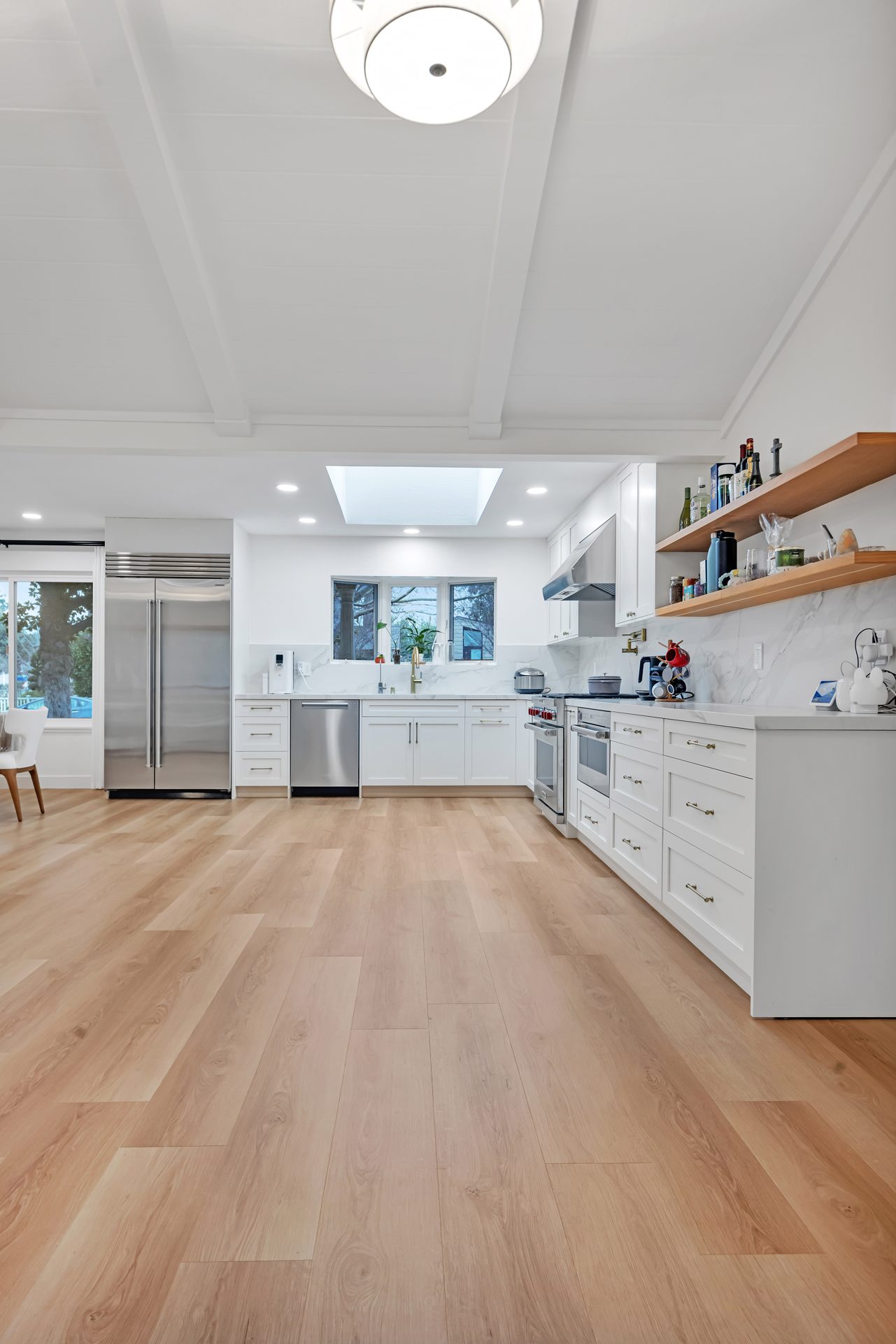 Remodeled white kitchen with stainless appliances, skylight and light wood-look flooring