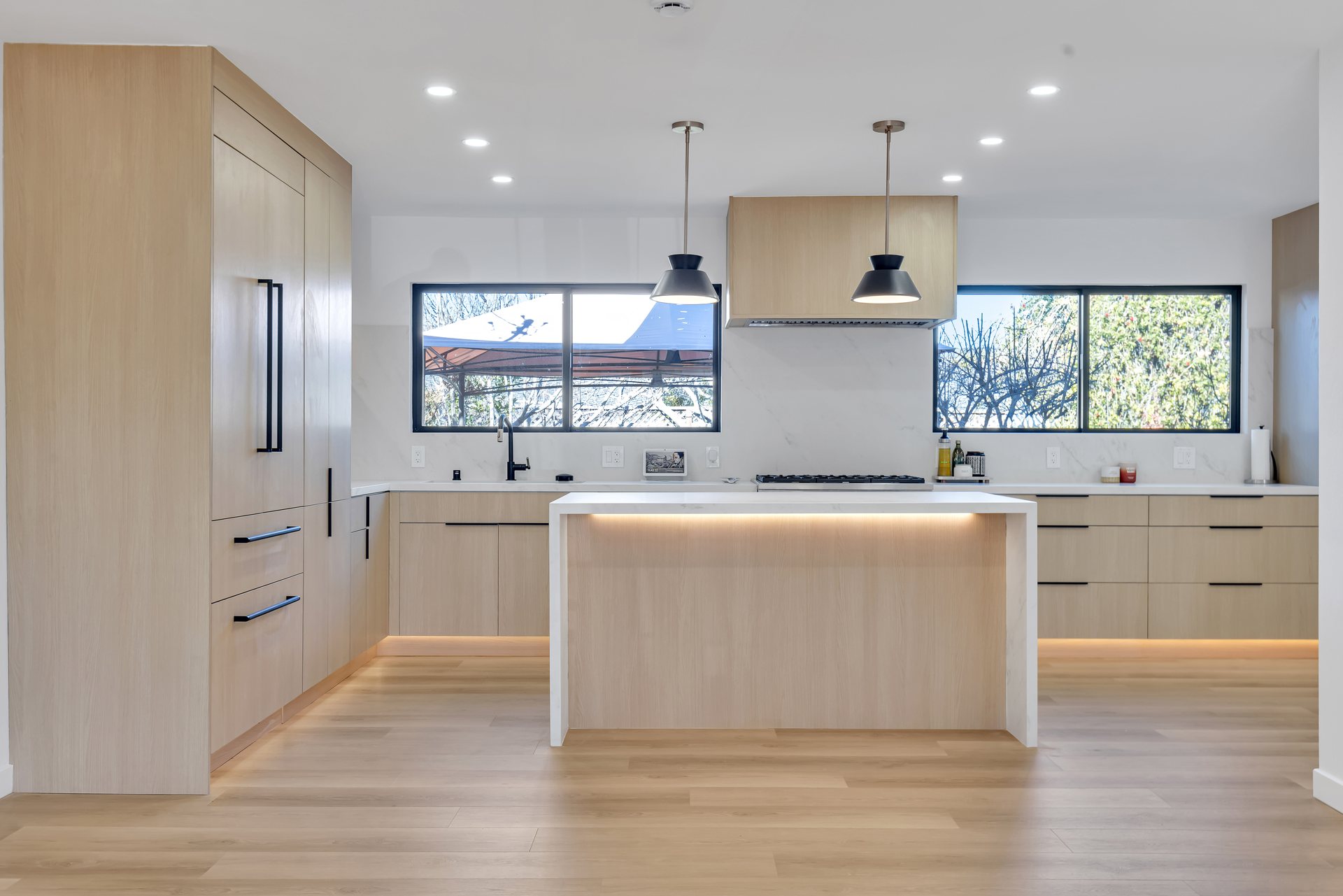 Light oak kitchen with a waterfall island, black pendant lights and under-cabinet lighting