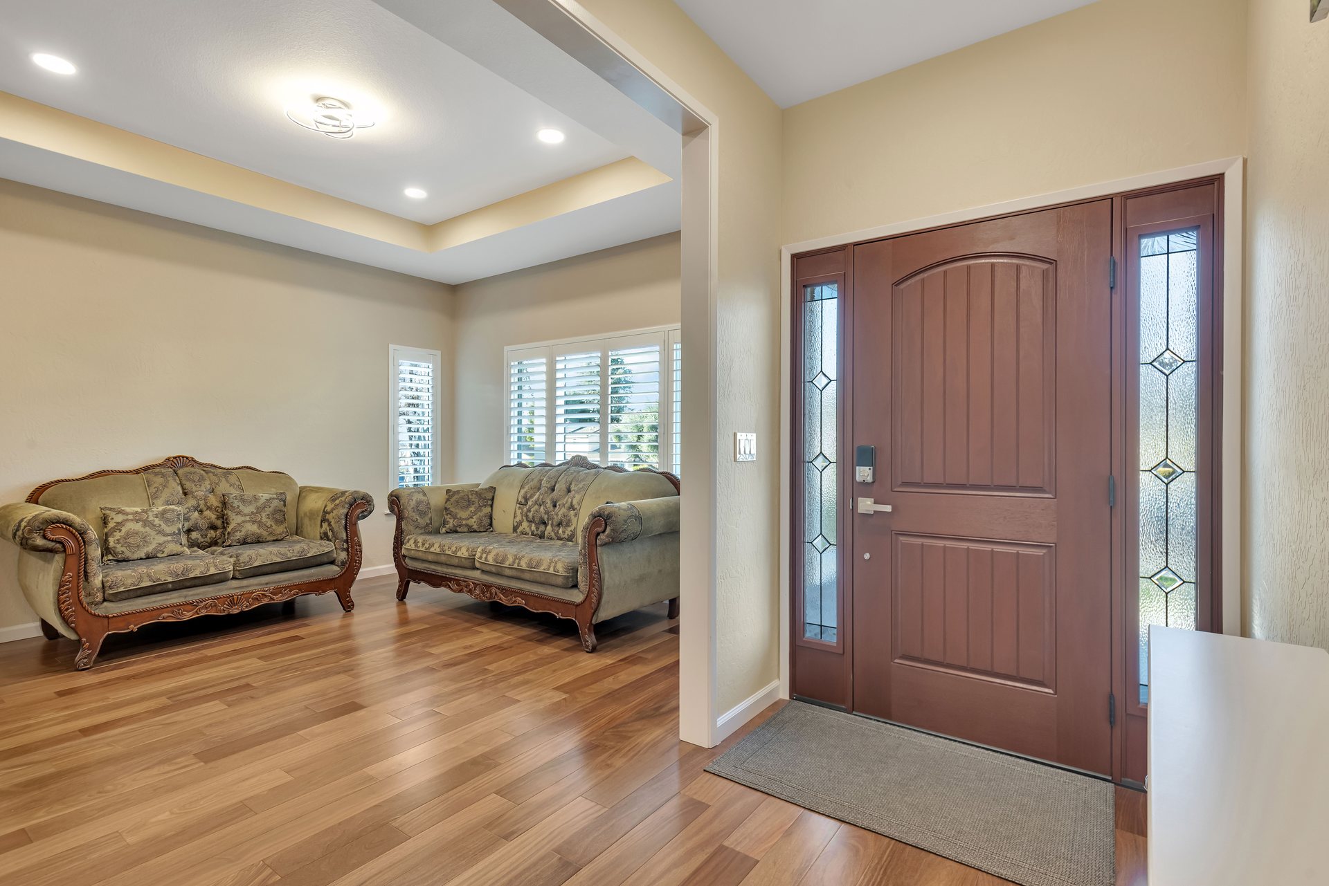 Living room with a tray ceiling, hardwood flooring and a front door with glass sidelights