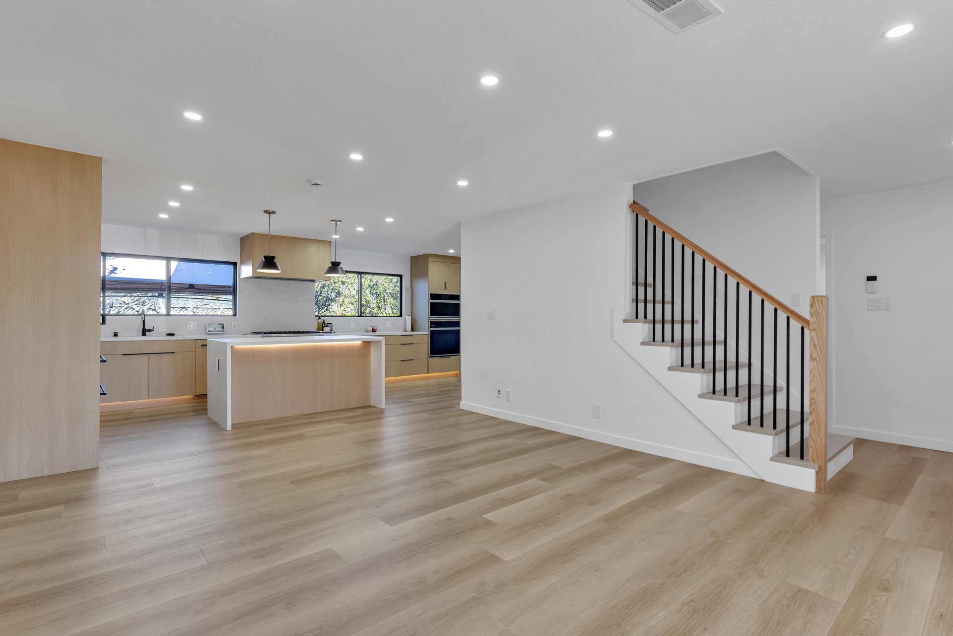 Open-plan living area with light wood-look flooring, a staircase and a kitchen island