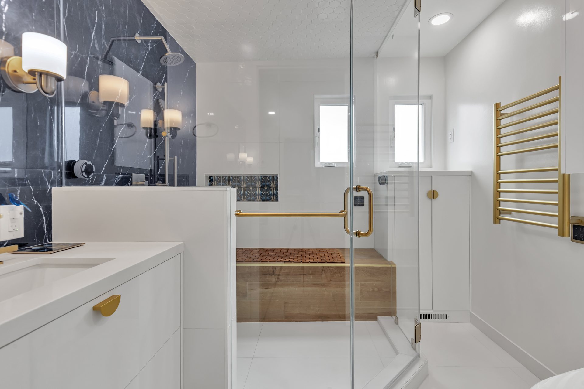 Remodeled bathroom with a frameless glass shower, wood-look bench and brushed brass fixtures
