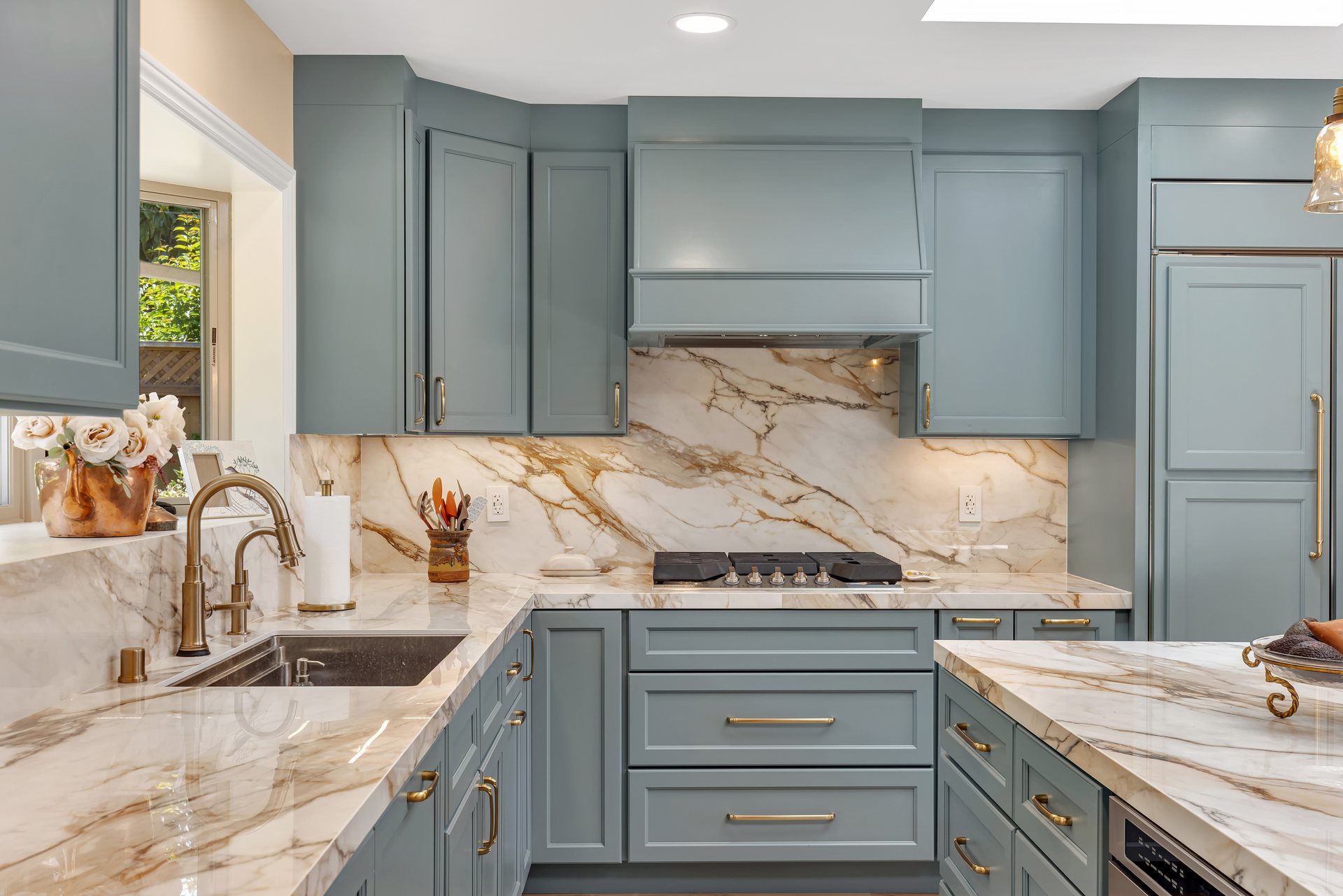 Range wall with a painted hood, marble slab backsplash and brass cabinet hardware